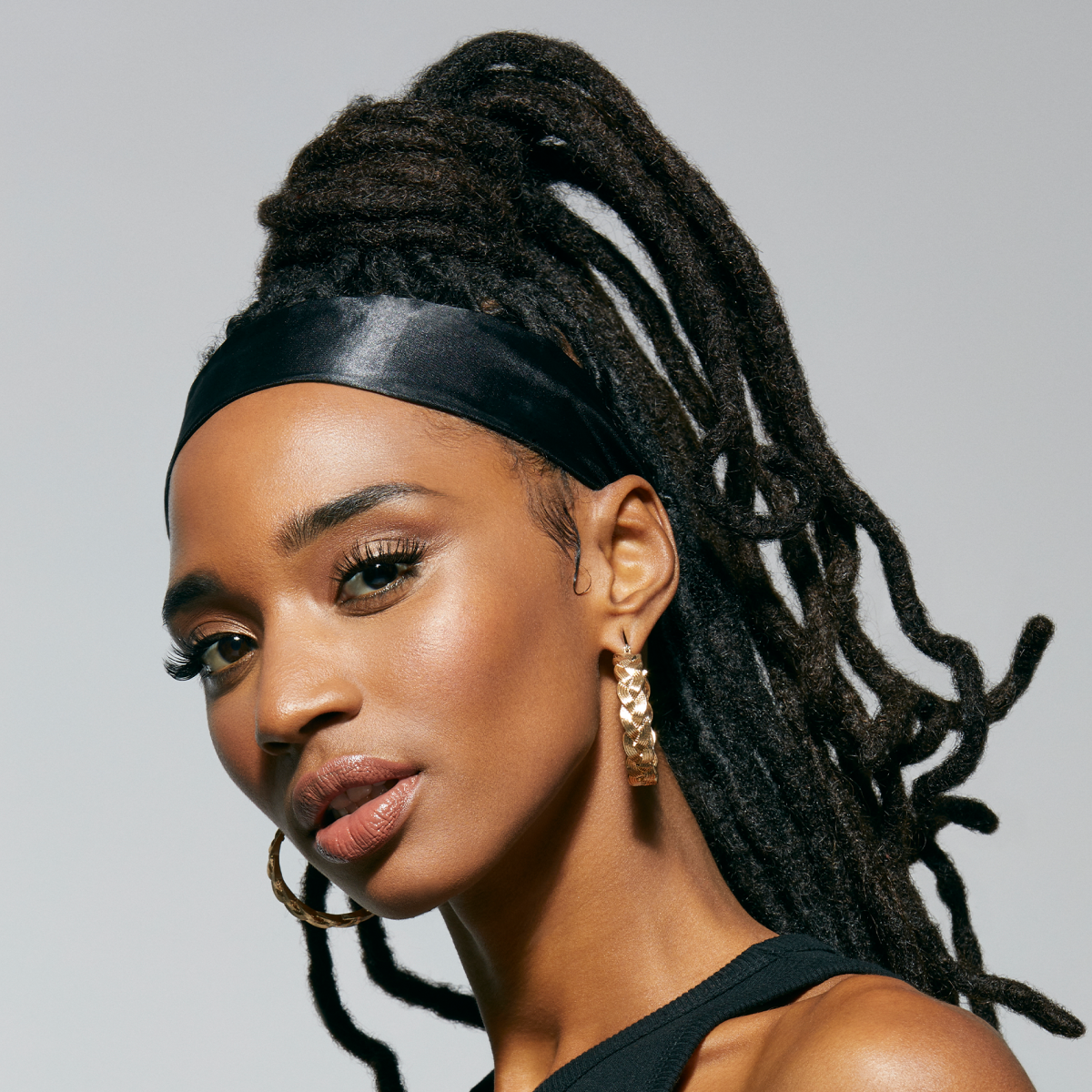 A black woman with long, shiny hair locs, looking stylish while laying down her edges with a Silky Satin black edge scarf from KISS Colors & Care.