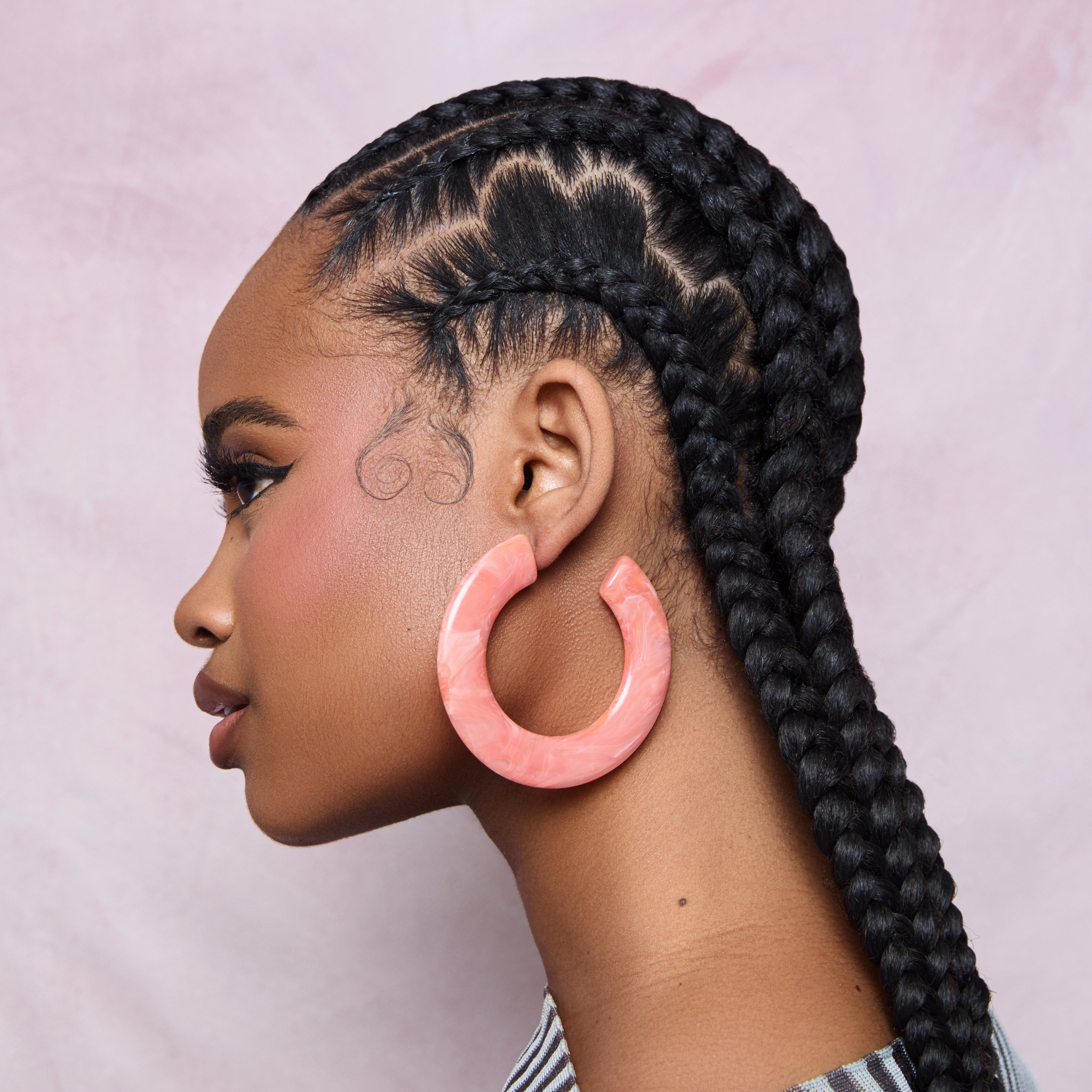 A woman showing off a design in her hair braids done by using the KISS Colors & Care Pin Tail Axe Parting Comb.
