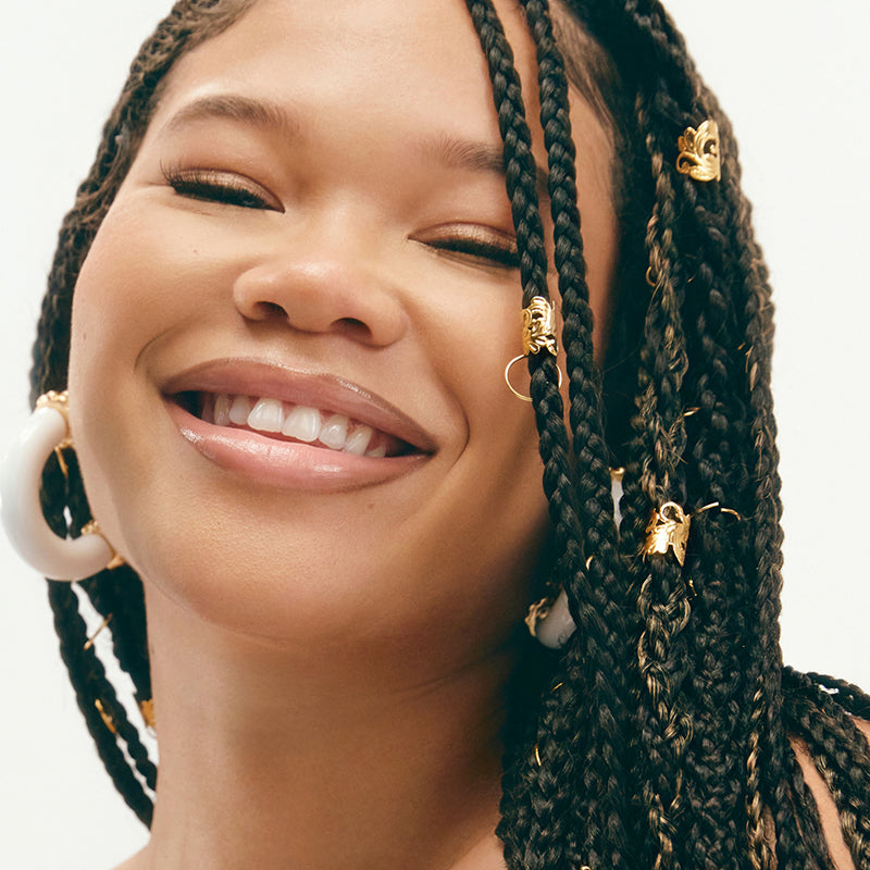 Actress Storm Reid featured smiling with braided hair and accented with gold hair beads