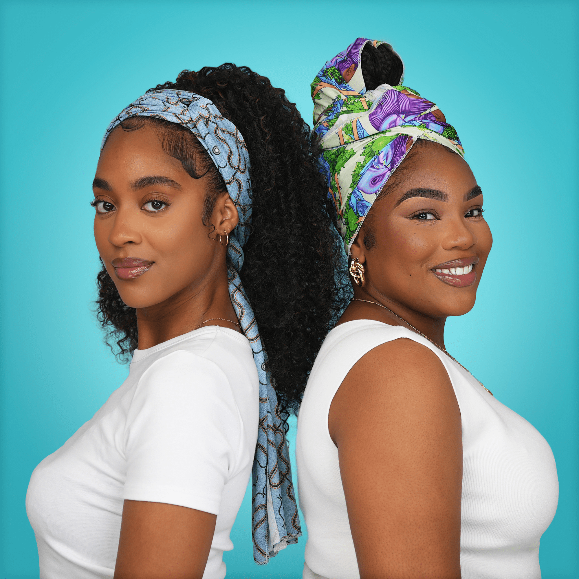 Two women stand back-to-back against a blue background, each wearing a colorful satin wrap scarf; one in blue patterned wrap, the other in a multicolored design.