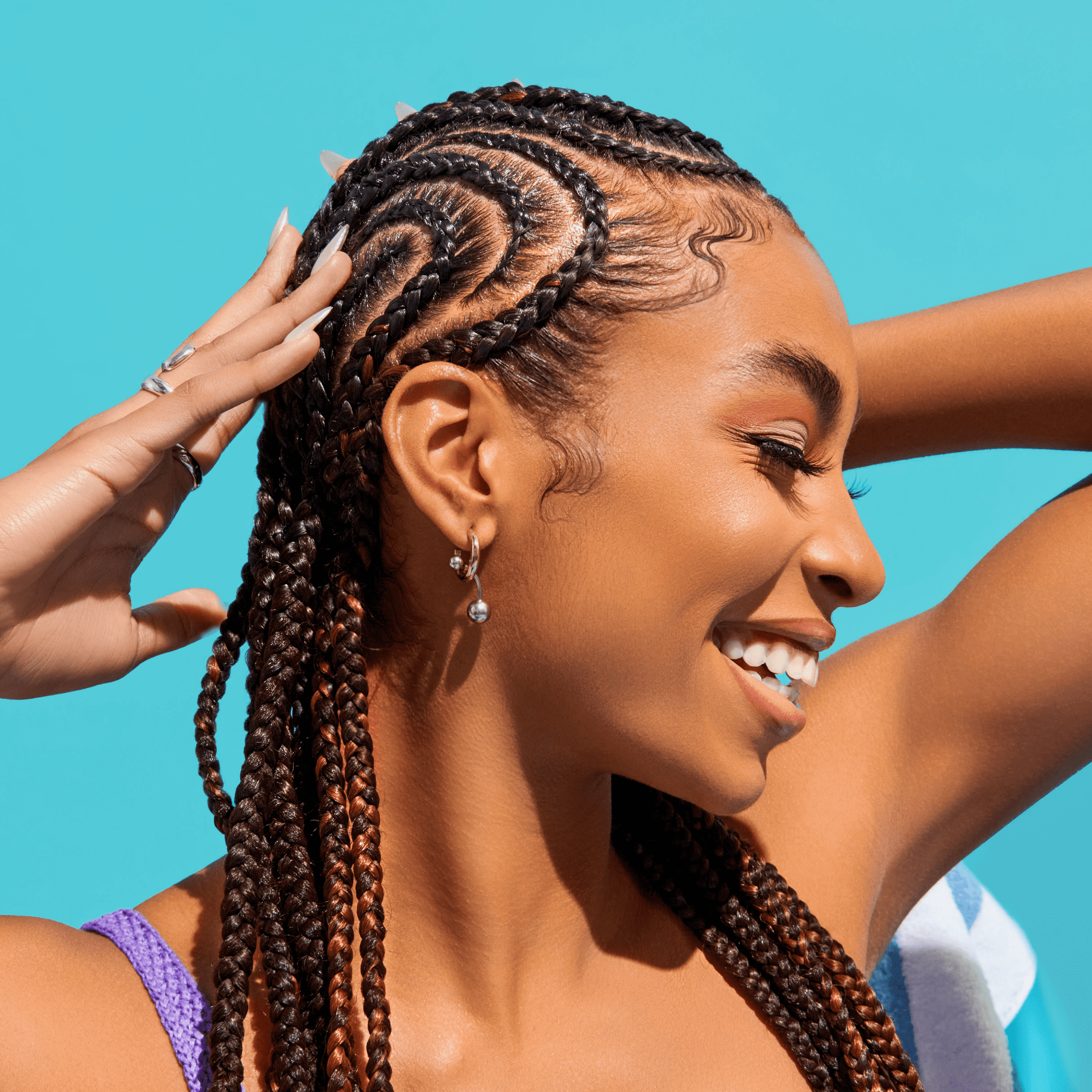 Smiling woman with intricately braided hair wearing a purple top against a bright blue background, showcasing healthy hair care results.