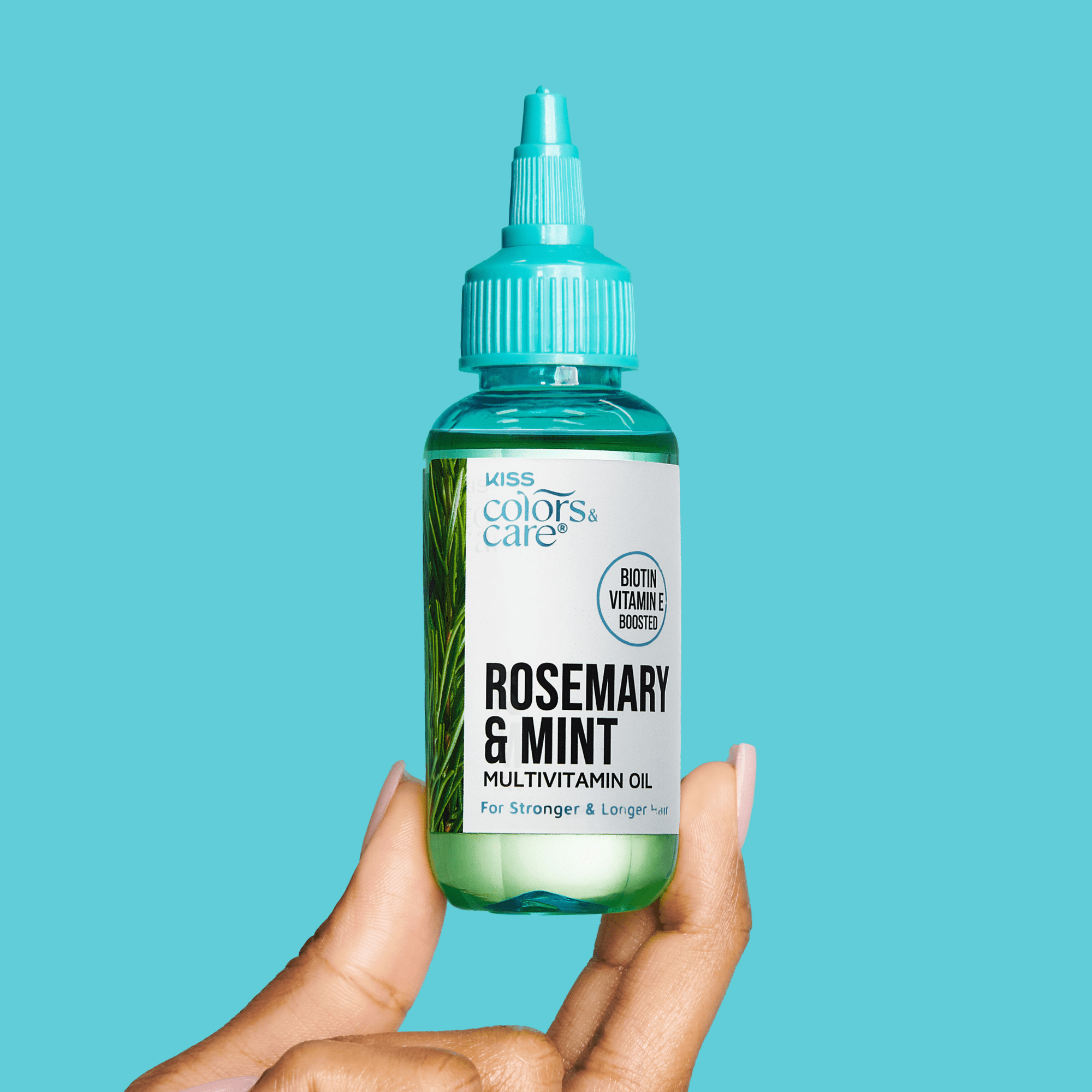 Hand holding a small clear green bottle with turquoise cap labeled "Rosemary & Mint Multivitamin Oil" from KISS Colors & Care, for stronger and longer hair.