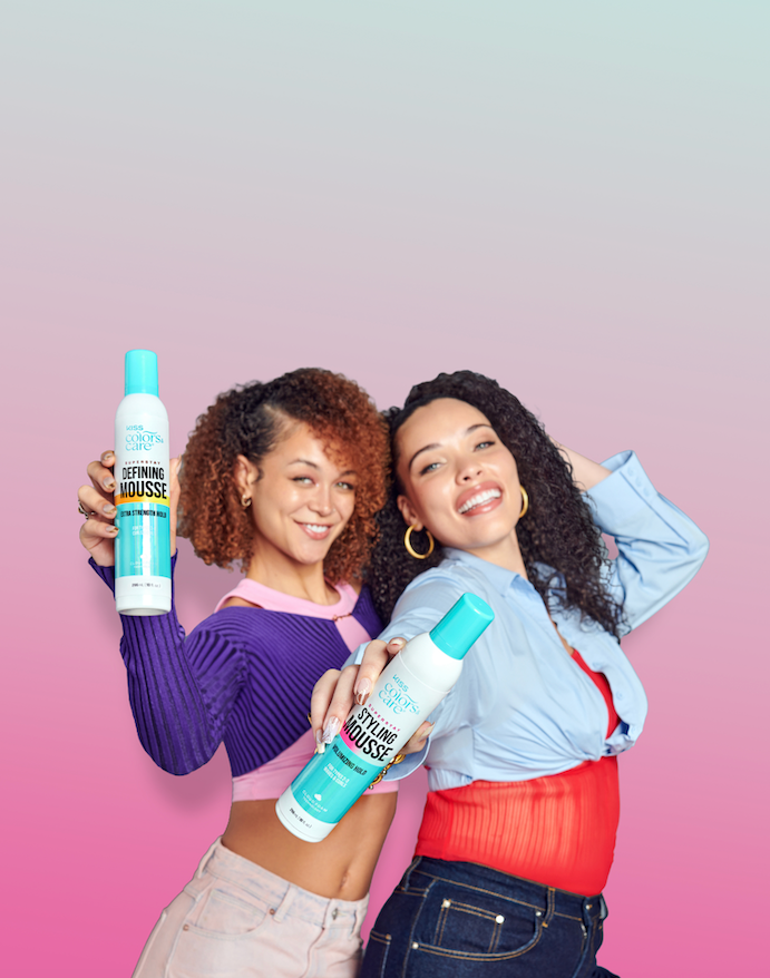 Two smiling women pose against a pink gradient background, each holding a bottle of L'Oréal Kiss Colors Care Styling Defining Mousse.