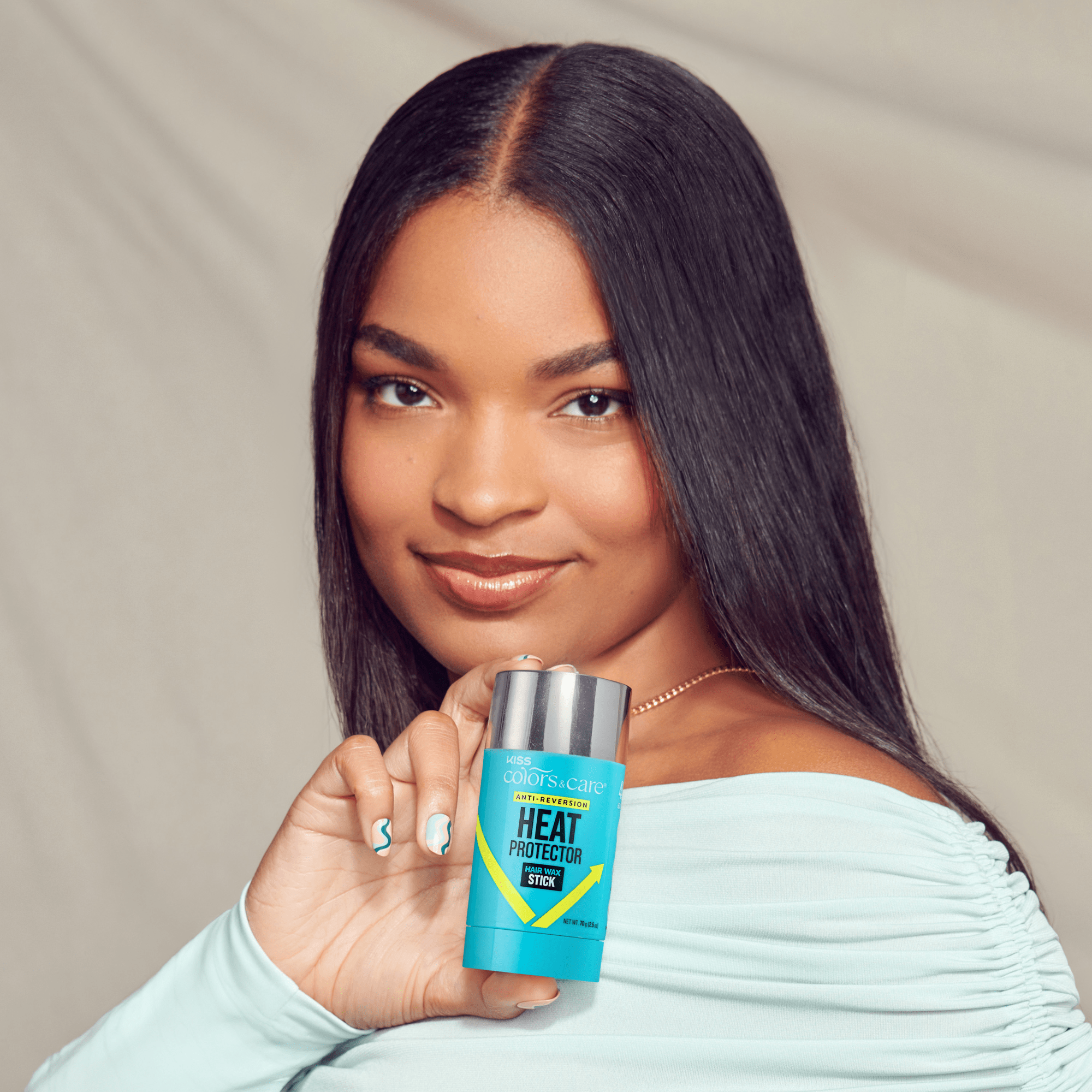 Woman with straight dark hair wearing a light blue top holds a blue KISS Colors & Care Heat Protector Hair Wax Stick labeled "Anti-Reversion."