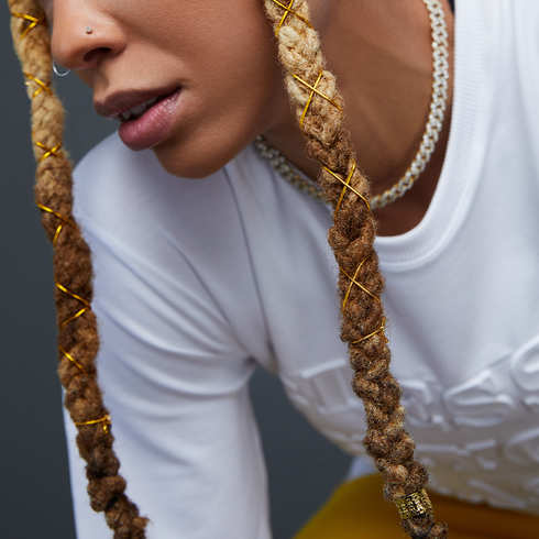A woman wearing braids that are decorated with gold braid charms from KISS Colors & Care.