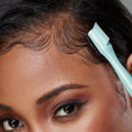 Close-up of a person using a light blue 4-in-1 edge boar brush to style baby hairs along the hairline.