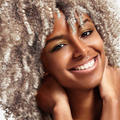 Close-up of a smiling woman with voluminous, bleached curly hair and glowing skin, showing the effect of a hair lift and care product.