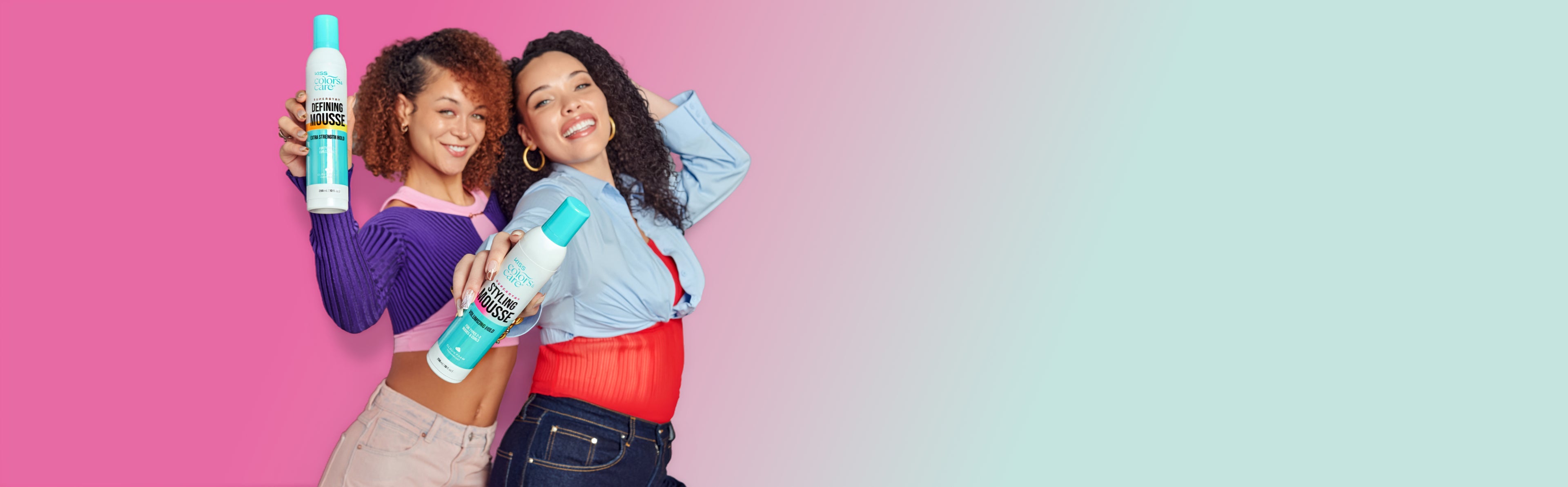 Two smiling women with curly hair holding colorful mousse hair product bottles against a split pink and blue background.