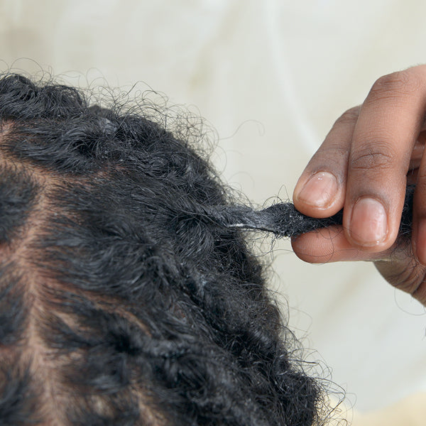 Person braiding their hair with dark hair extensions against a neutral background