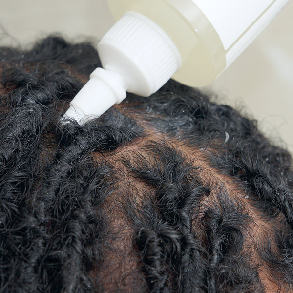 Person applying a white bottle of product to their hair, with a focus on the hair and product.