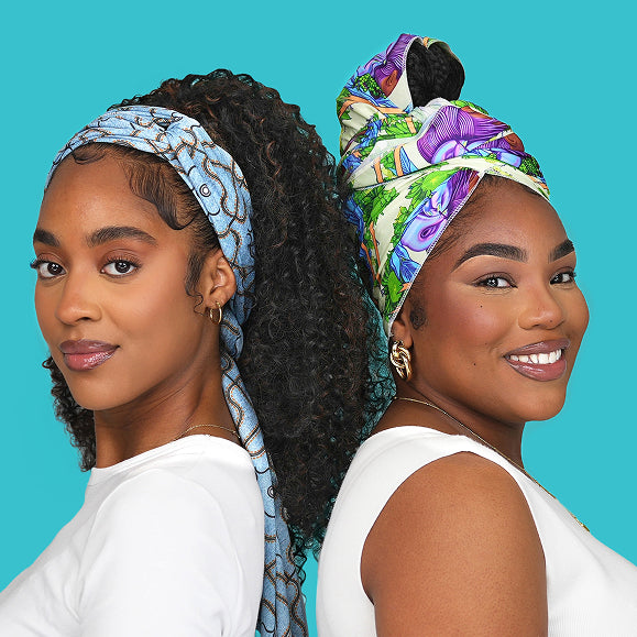 Two women wearing colorful patterned headwraps and gold hoop earrings, smiling against a turquoise background.