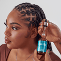 Woman with braided hair holds open dropper bottle of Scalp Fixer serum with turquoise label stating "Strengthening Hair &amp; Scalp Serum" and benefits: encourages growth, revitalizes roots, relieves tension.