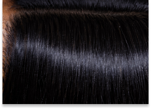 Close-up of a section of shiny, smooth black hair with a visible middle parting, showing healthy strands and scalp.