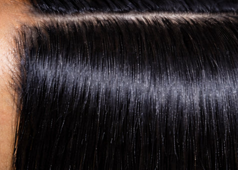 Close-up of smooth, shiny black hair parted neatly with visible scalp and fine strands, highlighting hair health and shine.