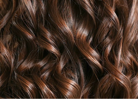 Close-up of shiny, wavy chestnut brown hair strands with natural highlights, showing smooth texture and healthy appearance.