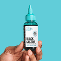 Hand holding a small clear bottle with turquoise dropper cap labeled "KISS Colors &amp; Care Black Castor Multivitamin Oil" for dry and flaky scalp, with biotin and vitamin E boosted.