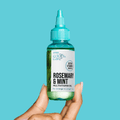 Hand holding a small clear green bottle with turquoise cap labeled "Rosemary &amp; Mint Multivitamin Oil" from KISS Colors &amp; Care, for stronger and longer hair.